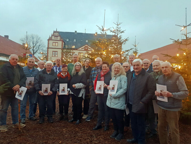 18 der insgesamt 28 Ortsheimatpflegerinnen und Ortsheimatpfleger der Stadt Salzgitter präsentieren bei ihrem Jahresabschlusstreffen mit Kulturdezernent Jan Erik Bohling und Dr. Claudia Böhler vom Stadtarchiv die druckfrische neue Broschüre vor der Kulisse des Winterwaldes im Schlosshof Salder.