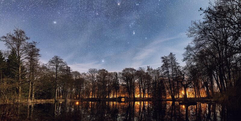 Auf dem Bild ist der Schlossteich des Schlosses Ringelheim bei Nacht zu sehen. Über dem Schlossteich sind viele Sterne zu sehen.